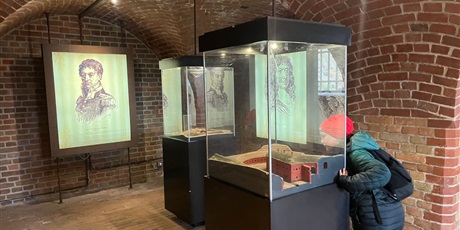 Powiększ grafikę: Uczeń ogląda eksponaty w muzeum w zabytkowym wnętrzu z cegły i gablotami