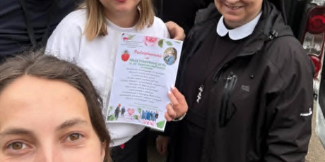 Powiększ grafikę: Grupa osób przed samochodem podczas przekazania darów, jedna osoba trzyma podziękowanie