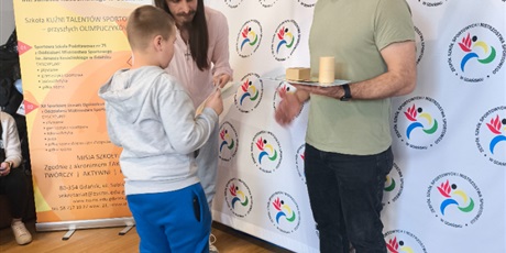 Powiększ grafikę: „Uczeń odbiera nagrodę od dwóch prowadzących podczas szkolnego wydarzenia sportowego w Gdańsku.”