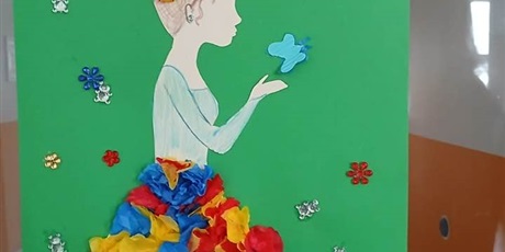 Powiększ grafikę: „Praca plastyczna przedstawiająca postać w sukni z kolorowej bibuły na tle zielonej planszy z napisem ‘Wiosna na Zielonym’.”