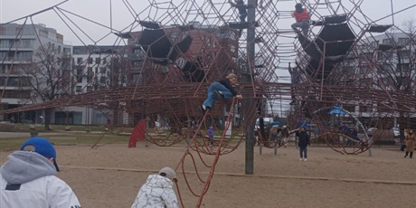 Powiększ grafikę: „Uczniowie przechodzą po linowej ścieżce prowadzącej do wysokiej konstrukcji do wspinania.”