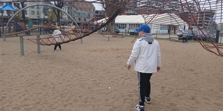 Powiększ grafikę: „Dzieci bawią się na linowym torze przeszkód na piaszczystym placu zabaw.”