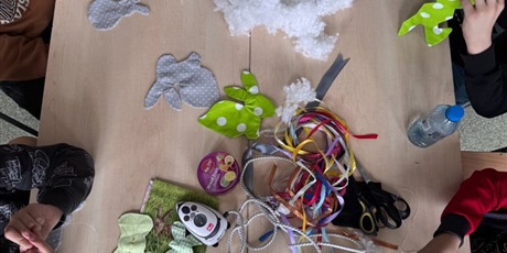 Powiększ grafikę: Dzieci szyją i wypełniają materiałowe zajączki przy stole pełnym przyborów plastycznych