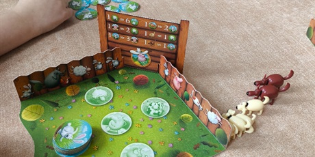 Powiększ grafikę: „Zbliżenie na planszę gry z ilustracjami zwierząt, żetonami i figurkami, podczas rozgrywki dzieci przy stole.”