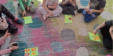 Powiększ grafikę: Dzieci siedzą w kręgu na kolorowym dywanie i wykonują wielkanocne prace plastyczne