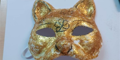 Powiększ grafikę: „Złota maska lisa z brokatem i narysowanymi detalami leży na kartce jako gotowa praca ucznia.”