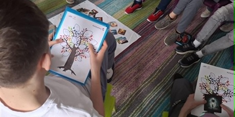 Powiększ grafikę: Uczniowie siedzą w kręgu i omawiają swoje karty pracy dotyczące zainteresowań i mocnych stron