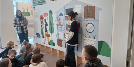 Powiększ grafikę: „Grupa dzieci uczestniczy w zajęciach edukacyjnych przy dużej planszy o tematyce ekologicznej i ograniczaniu odpadów.”