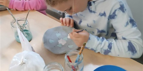Powiększ grafikę: Dziewczynka pracuje przy stoliku z klejem i materiałami.