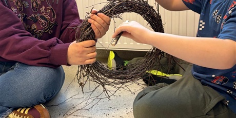 Powiększ grafikę: „Dzieci formują okrągły wianek z cienkich gałązek, przygotowując bazę do wielkanocnej dekoracji.”