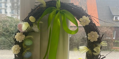 Powiększ grafikę: „Gotowy wielkanocny wianek z gałązek ozdobiony wstążką, pisankami i kurczaczkami zawieszony na oknie.”